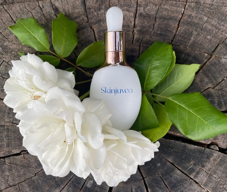 Skinjuvea dropper bottle surrounded by white flowers and green leaves on a wooden surface.