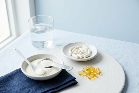 Supplement capsules, softgels, collagen powder and a glass of water on a white table