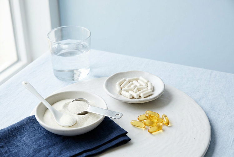 Supplement capsules, softgels, collagen powder and a glass of water on a white table